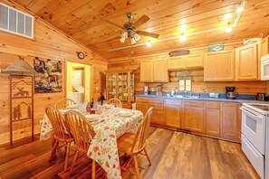 A wooden cabin interior with a dining area, kitchen, and a ceiling fan.