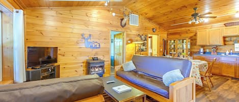 A cozy cabin interior with a wooden interior, a sofa, a television, a fireplace, and a kitchen area.
