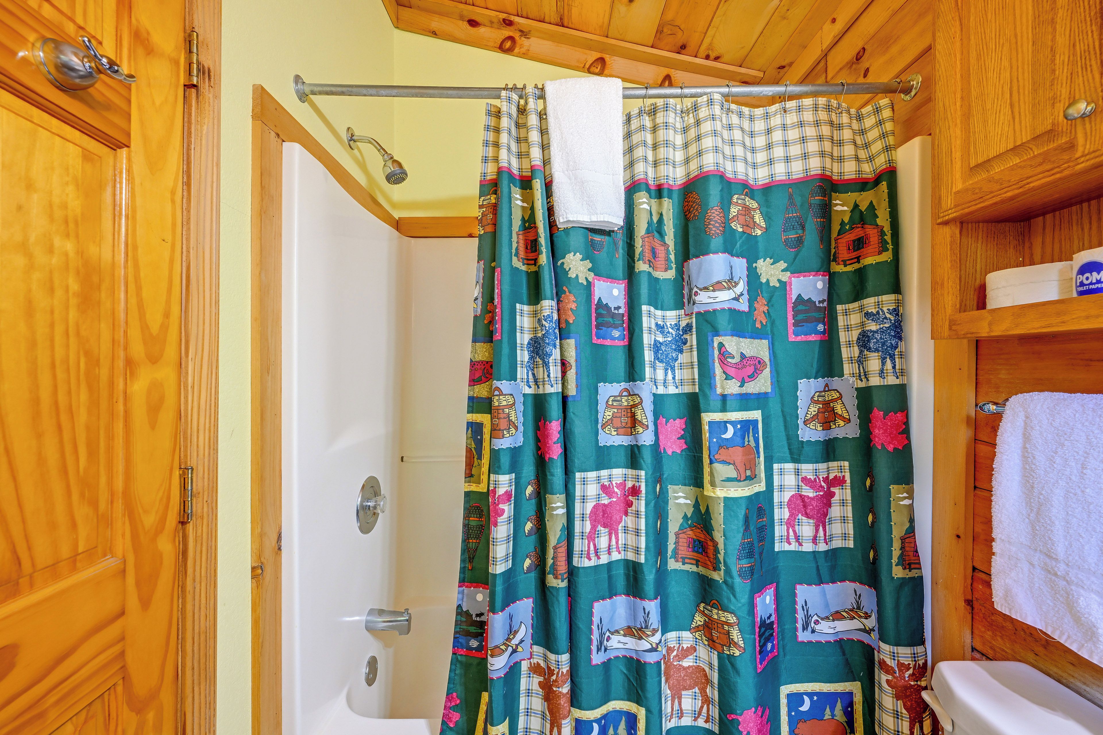 Un baño con puerta de madera, una bañera blanca y una cortina de ducha con diseño estampado.