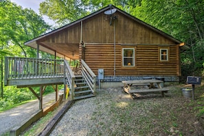 Eine rustikale Holzhütte mit einer Holzterrasse, einem Picknicktisch und einer Fundamentmauer aus Stein.