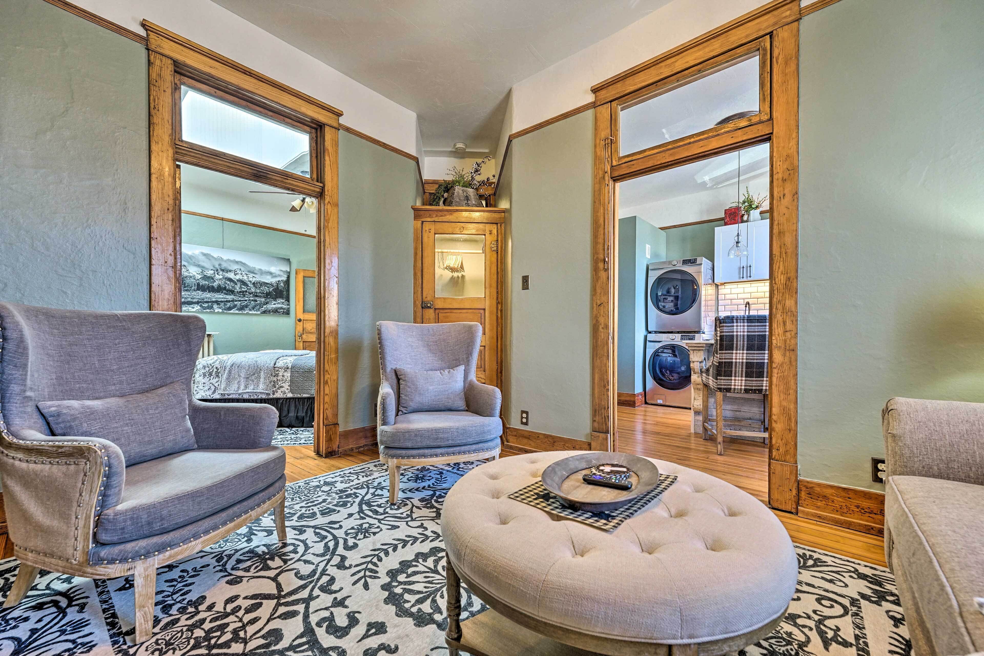 A living room with two armchairs, a round ottoman, and a patterned rug.