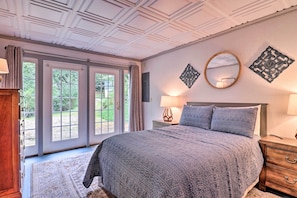 A bedroom with a large bed, a wooden nightstand, a mirror, and a window with a view of greenery. - Family Retreat Cabin w/ Summit, Lake Views, Deck! (Topton)