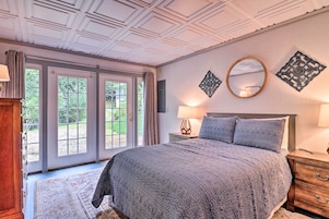 Quarto com cama grande, mesa de cabeceira de madeira, espelho e janela com vista para o verde.