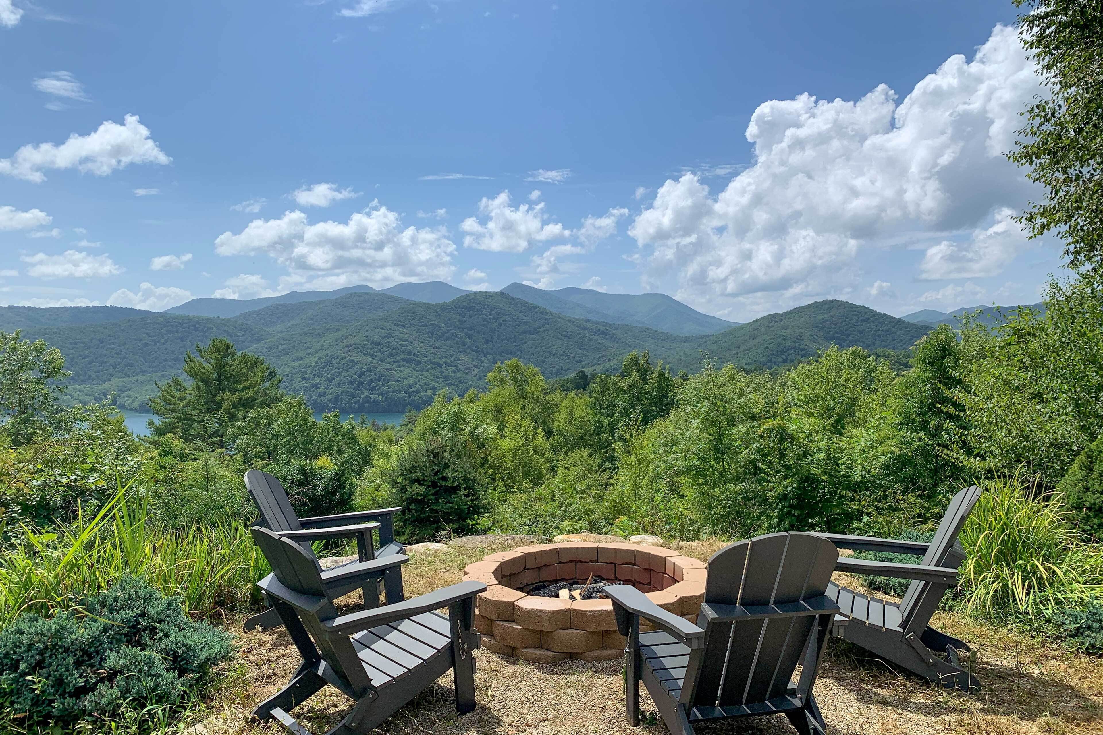 A view of a mountainous landscape with a fire pit and two Adirondack chairs.
