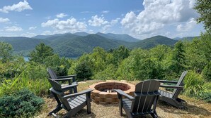 A view of a mountainous landscape with a fire pit and two Adirondack chairs.