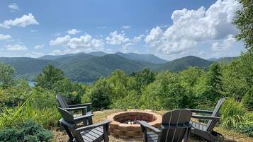 A view of a mountainous landscape with a fire pit and two Adirondack chairs.