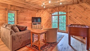A cozy wooden cabin interior with a sofa, a table, a television, and a foosball table.