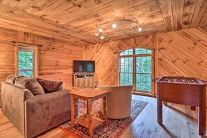 A cozy wooden cabin interior with a sofa, a table, a television, and a foosball table.