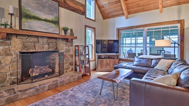 A cozy living room with a stone fireplace, leather sofa, and a large window.