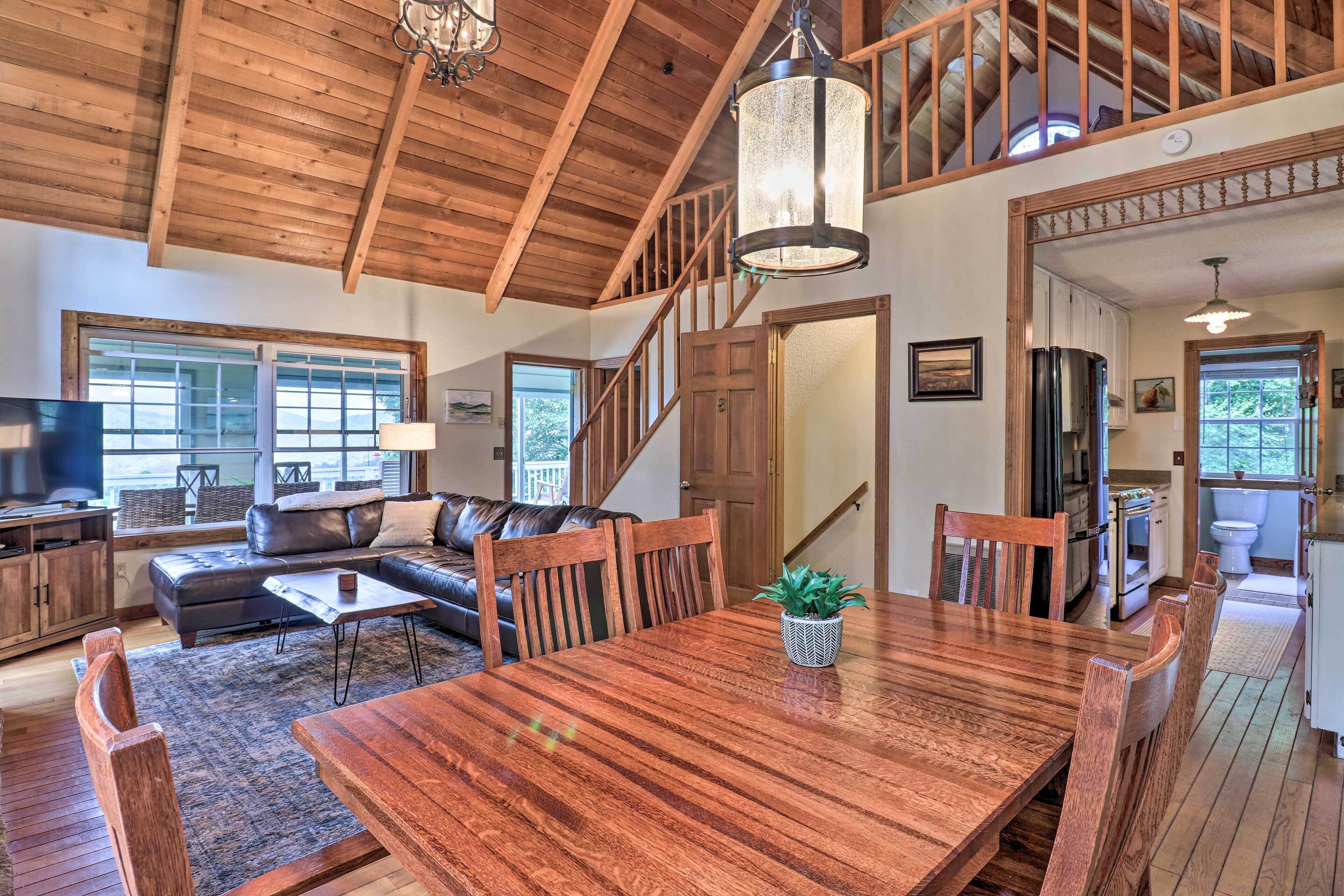 A spacious living room with a wooden dining table, a sofa, and a staircase leading to an upper level.