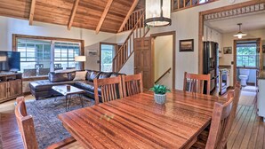 A spacious living room with a wooden dining table, a sofa, and a staircase leading to an upper level.