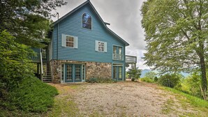 A large, two-story house with a stone foundation and blue siding, featuring a front porch and a balcony.