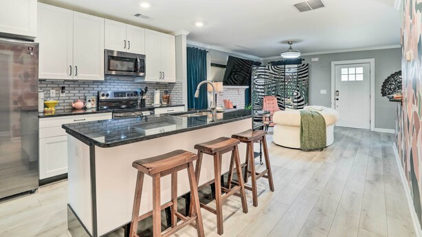 A modern kitchen with white cabinets, a black countertop, and wooden stools. - Eclectic Atlanta Abode < 3 Mi to Downtown! (Atlanta)