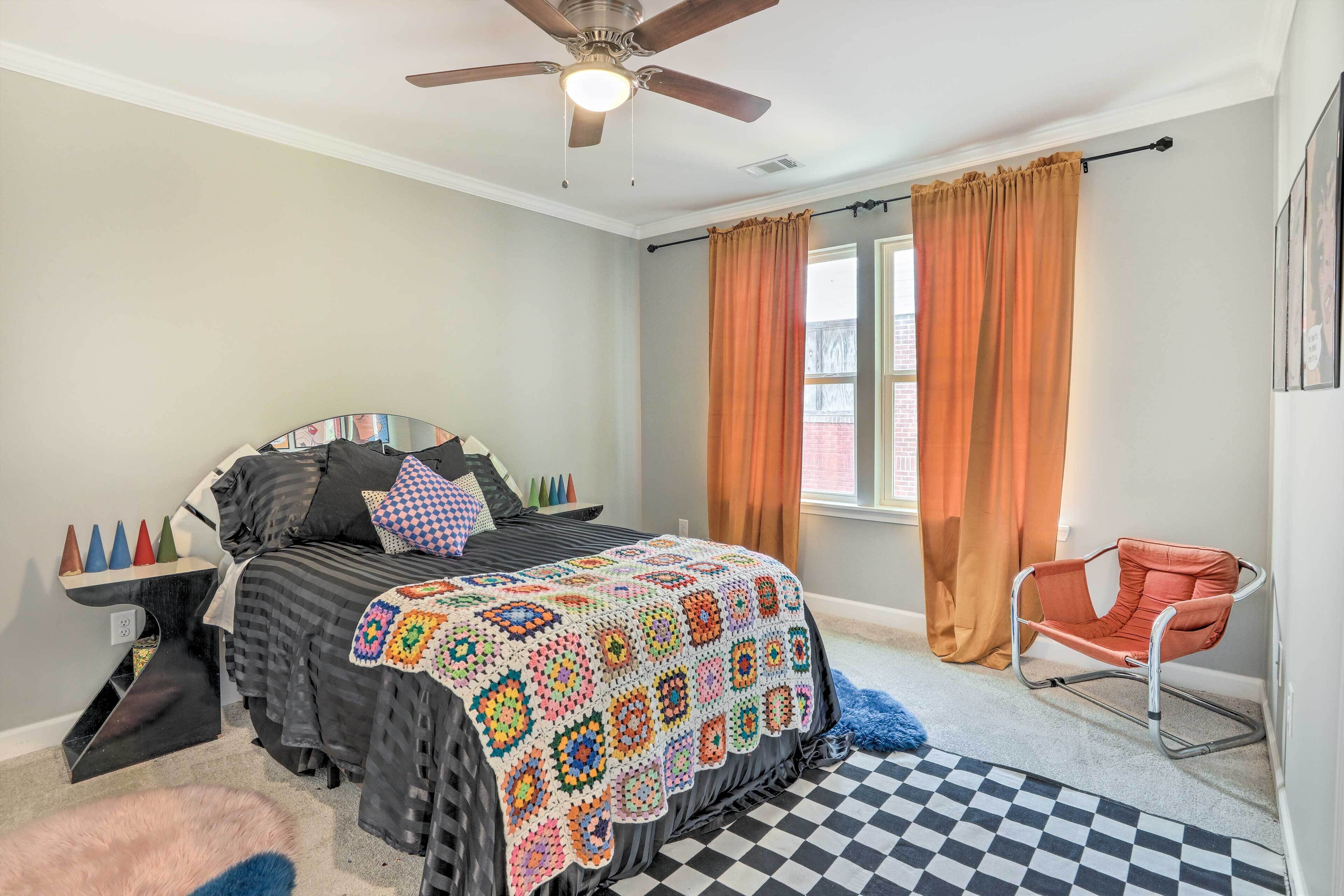 Une chambre à coucher avec un lit, un fauteuil à bascule, un ventilateur de plafond et une fenêtre avec des rideaux.