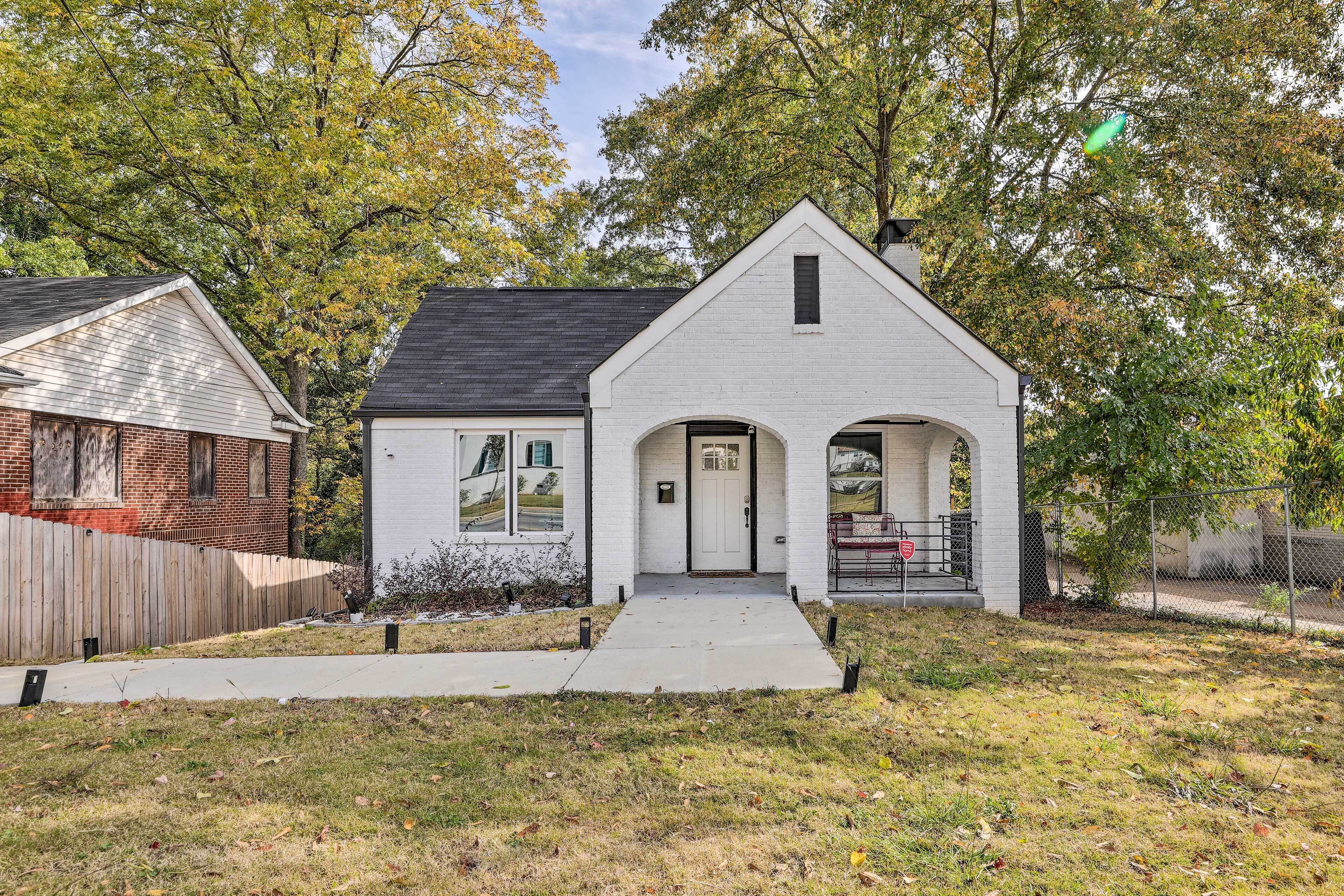 A single-story house with a white exterior, a black roof, and a front porch with two columns.