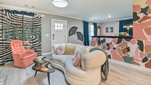A living room with a sofa, a pink armchair, a coffee table, and a decorative wall with abstract patterns. - Eclectic Atlanta Abode < 3 Mi to Downtown! (Atlanta)