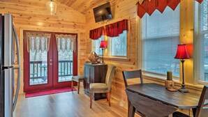 A wooden cabin interior with a dining table, chairs, a TV mounted on the wall, and a red door with glass panels. - Cozy Heber Springs Cabin w/ Deck & Dock! (Heber Springs)