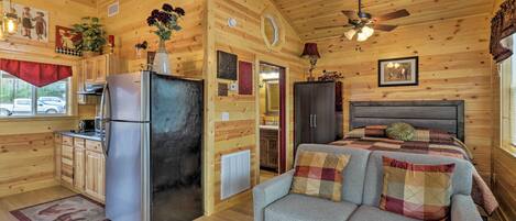 Interior de una cabaña con kitchenette, cama y sofá.