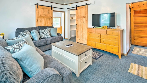 A modern living room with a sofa, coffee table, TV, and wooden cabinets. - Historic Cabin Retreat: Steps to Okoboji Lake (Arnolds Park)