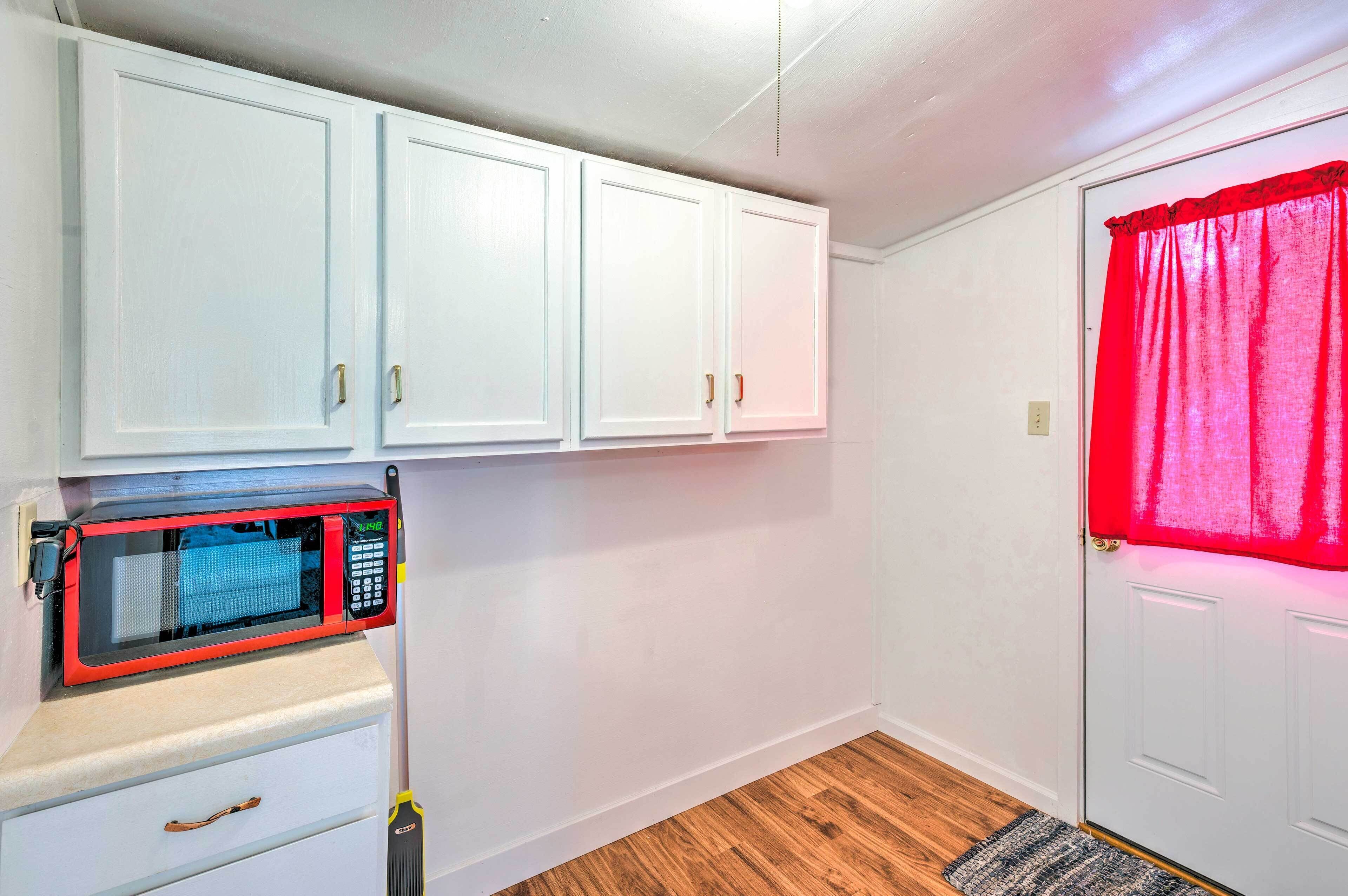 Une cuisine de taille réduite avec des meubles blancs, un four à micro-ondes et un rideau rouge sur une porte.