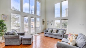 A spacious living room with large windows, grey sofas, and a wooden floor.