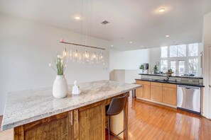 A modern kitchen with a marble countertop, wooden cabinets, stainless steel appliances, and a hanging light fixture.