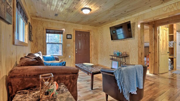 A wooden interior with a brown leather sofa, a small table with a bowl, and a television mounted on the wall.
