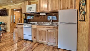 A wooden-paneled kitchen with a stove, microwave, refrigerator, and wooden cabinets.