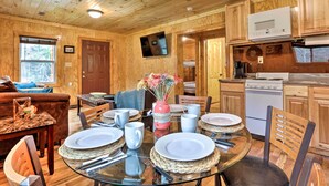 A wooden cabin interior with a dining area, kitchen, and living room.