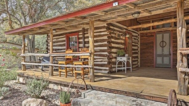 A rustic log cabin with a wooden porch, a dining table, and a potted plant. - 'gruene Cabin' - Pet Friendly New Braunfels Studio (New Braunfels)