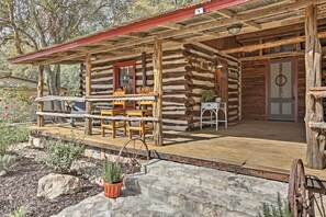 A rustic log cabin with a wooden porch, a dining table, and a potted plant. - 'gruene Cabin' - Pet Friendly New Braunfels Studio (New Braunfels)