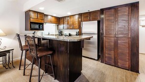 A kitchen with dark wooden cabinets, a stainless steel refrigerator, a microwave, and a granite countertop.