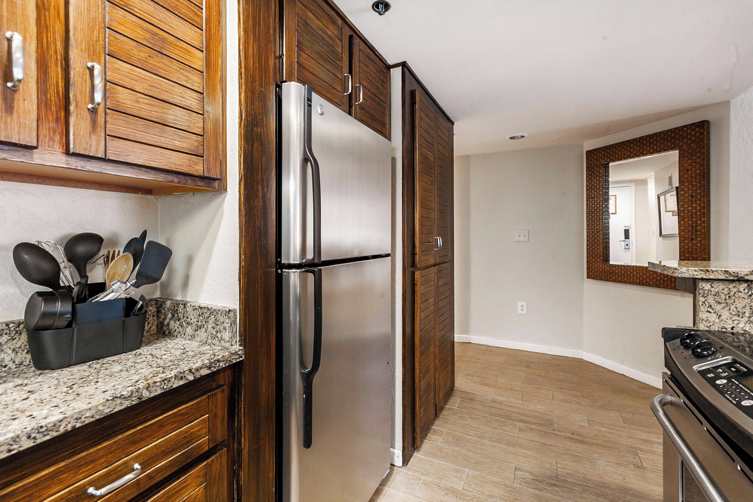 A modern kitchen with wooden cabinets, a stainless steel refrigerator, a granite countertop, and a built-in oven.
