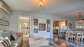 A spacious living area with a sofa, a coffee table, and a dining table with chairs. There is a kitchen area with cabinets and a chandelier.