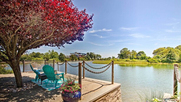 A lakeside patio with a table and chairs, a large flower pot, and a chain-link fence overlooking the water.