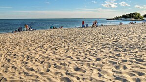 A sandy beach with people sunbathing and swimming.