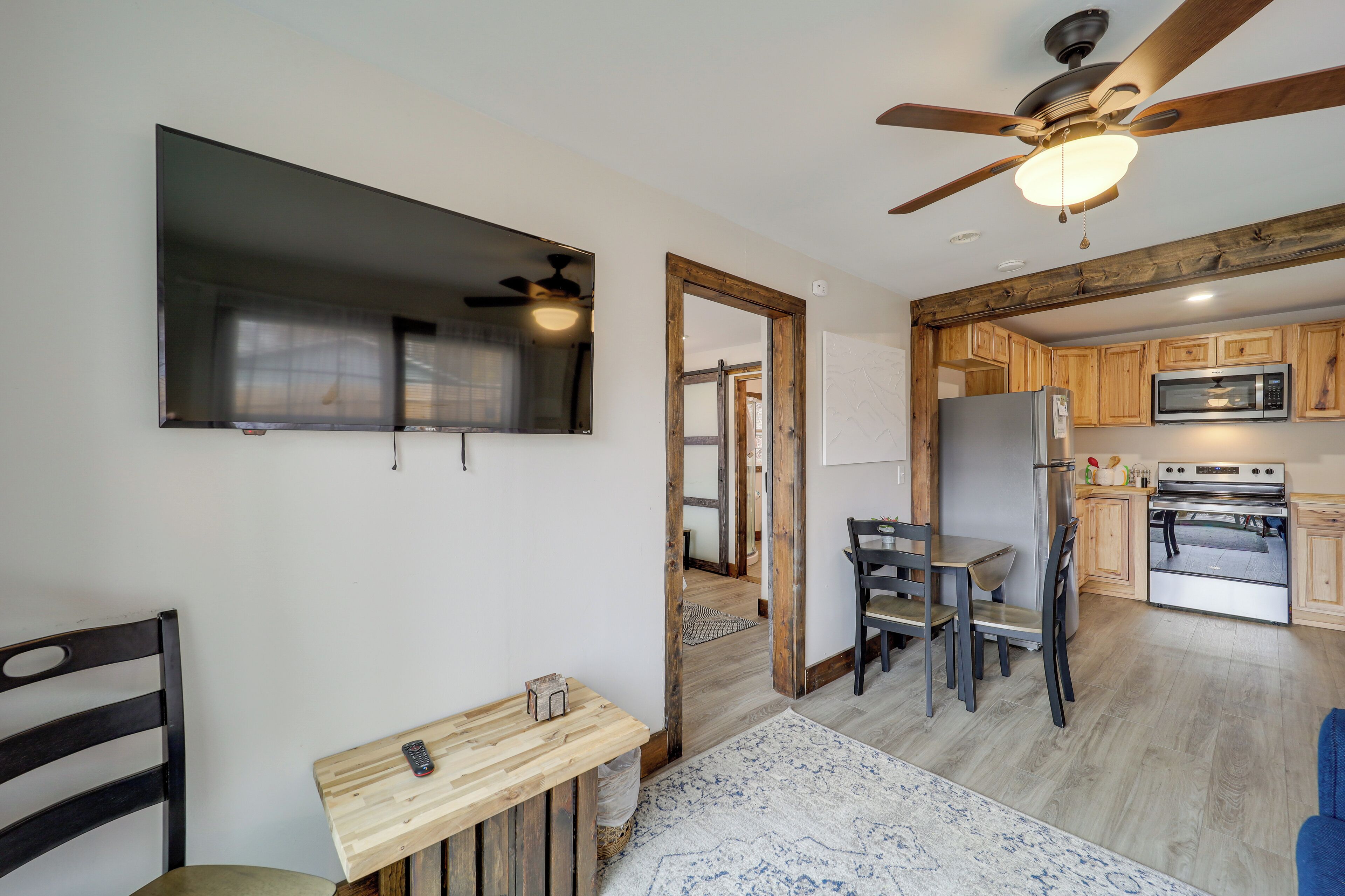 Una cocina moderna con armarios de madera, microondas y refrigerador. Hay un comedor con una mesa y sillas, y un ventilador de techo.