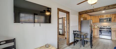 Una cocina moderna con armarios de madera, microondas y refrigerador. Hay un comedor con una mesa y sillas, y un ventilador de techo.