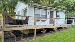 Ein Haus mit einer Holzterrasse, einem umzäunten Vorbereich und einem kleinen Garten.