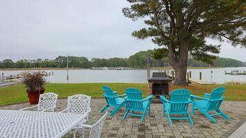 A patio with outdoor seating, a grill, and a view of a lake.