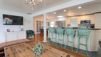 A spacious living area with a wooden dining table, a television, and a chandelier.