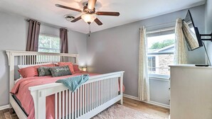 A bedroom with a white crib, a ceiling fan, a window with curtains, and a view of a brick building outside. - 5 Mi to Fort Hood! Brooklyn House w/ Fenced Yard (Killeen)