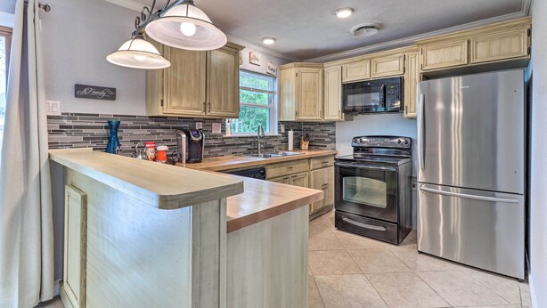 A modern kitchen with wooden cabinets, stainless steel appliances, a central island, and a hanging light fixture. - 5 Mi to Fort Hood! Brooklyn House w/ Fenced Yard (Killeen)