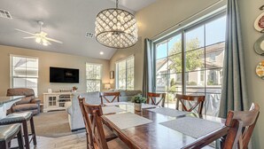 Un salon spacieux avec une grande table à manger, des sièges confortables, un ventilateur de plafond et une grande fenêtre donnant sur l’extérieur.