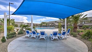 Un espace aménagé au bord de la piscine, avec des chaises longues sous un auvent bleu, une piscine et des jardins environnants.