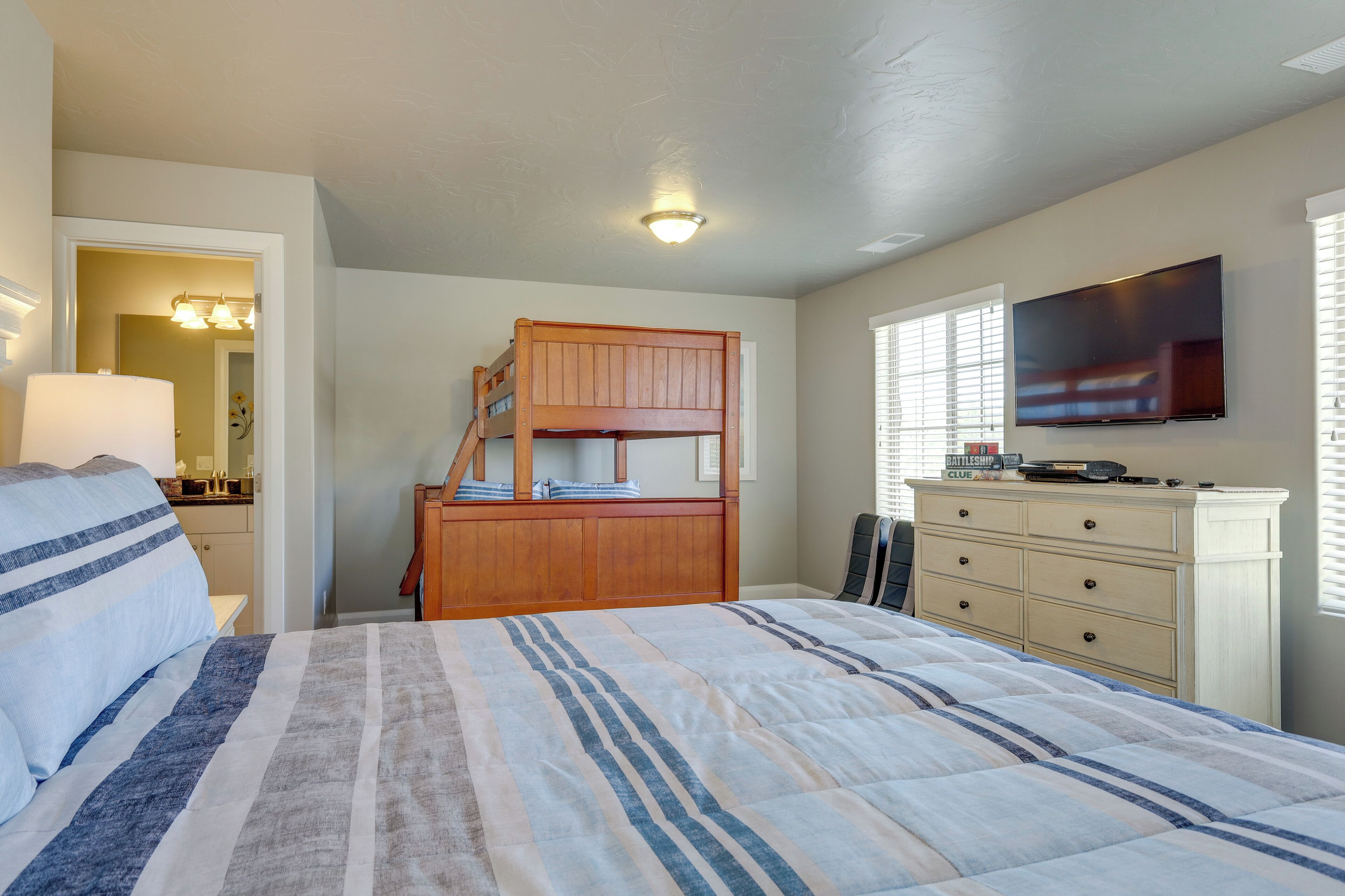 A bedroom with a bunk bed, a dresser, a TV, and a bedside lamp.