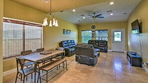 A spacious living room with a dining area, leather sofas, a ceiling fan, and a TV mounted on the wall. - Walk to Ocean: Lakefront Dickinson Stucco House! (Dickinson)