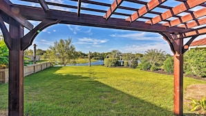 A wooden pergola structure in a well-maintained grassy yard with a clear sky. - Walk to Ocean: Lakefront Dickinson Stucco House! (Dickinson)