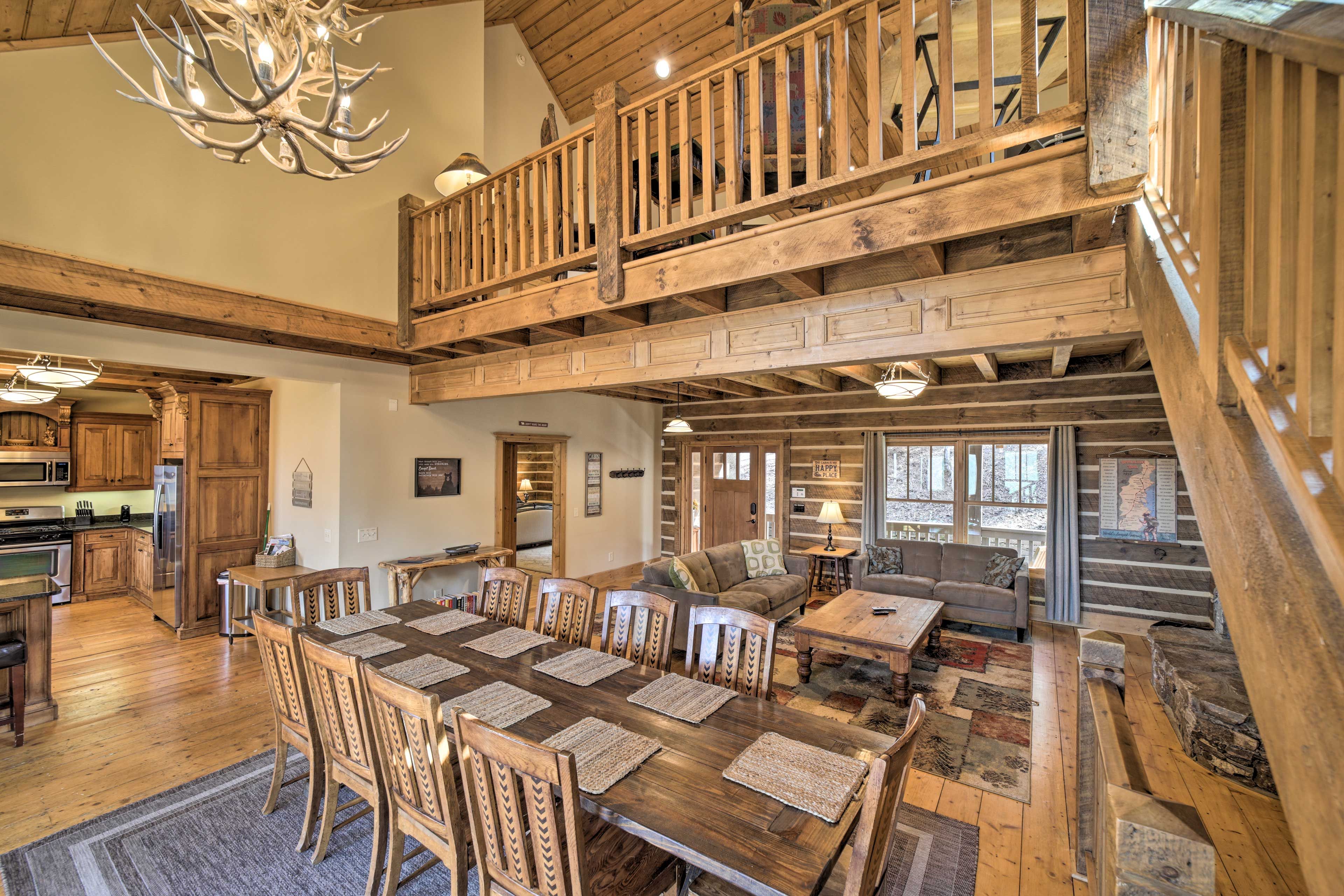Un comedor amplio con una larga mesa de madera y sillas, una cocina con armarios de madera, y una escalera que conduce a un nivel superior.