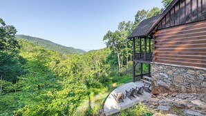 A wooden cabin with a stone foundation, a balcony with outdoor seating, and a view of a forested mountain. - Hot Tub + Pool Table: Cozy Franklin Cabin! (Franklin)